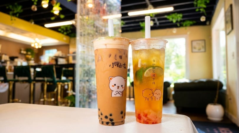 Two bubble tea drinks, one milk tea and one fruit tea, on a table in a cafe.