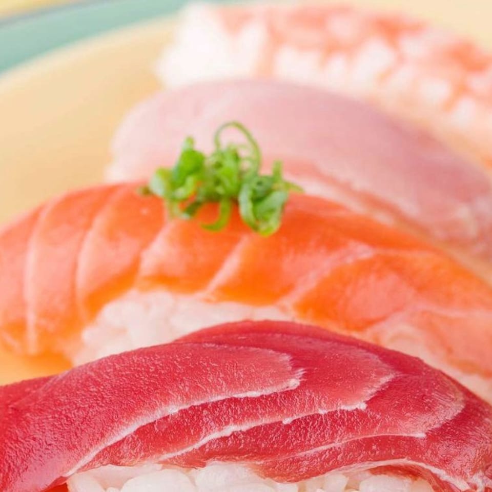 Four pieces of colorful nigiri sushi with tuna, salmon, and shrimp on a yellow plate.