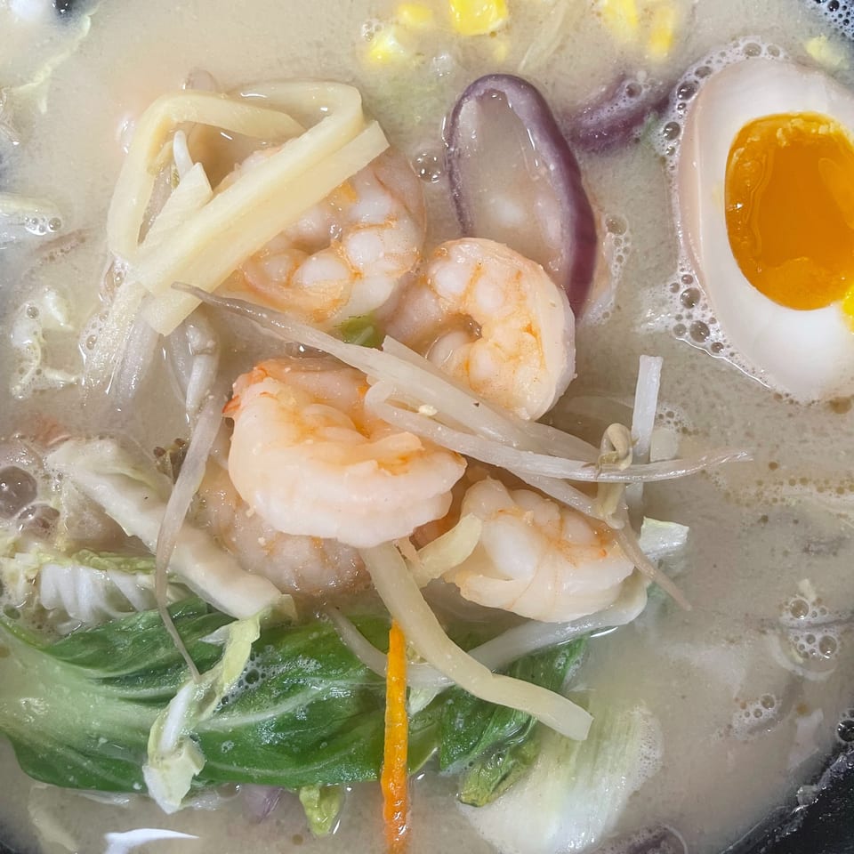 Close-up of a creamy ramen bowl with shrimp, corn, soft-boiled egg, and vegetables.