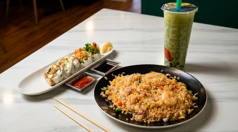 Sushi rolls, shrimp fried rice, and a green bubble tea on a white marble table.